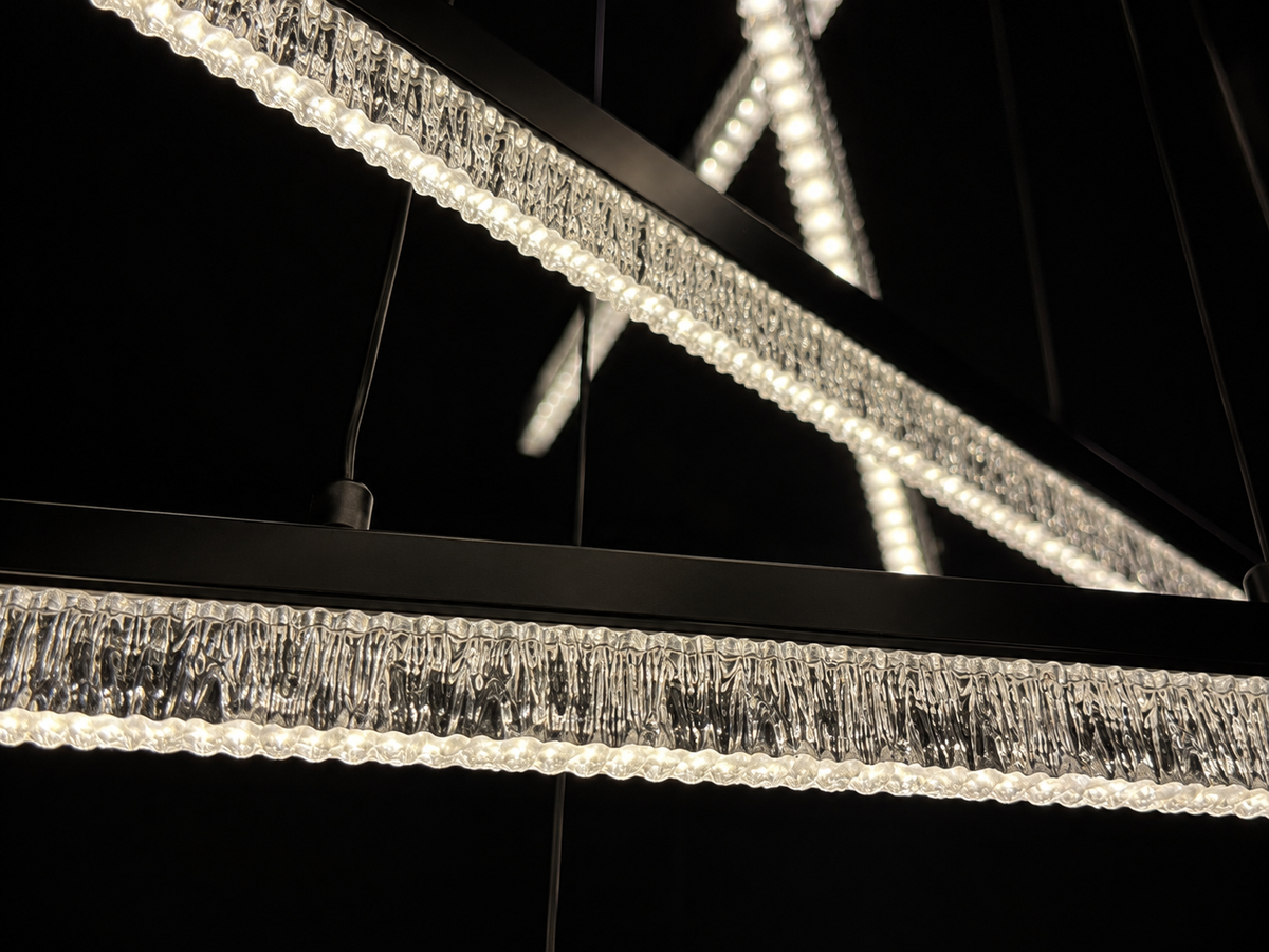 Modern linear LED chandelier with a textured clear crystal drip fringe and a matte black frame, shown illuminated against a dark background.