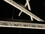 Modern linear LED chandelier with a textured clear crystal drip fringe and a matte black frame, shown illuminated against a dark background.