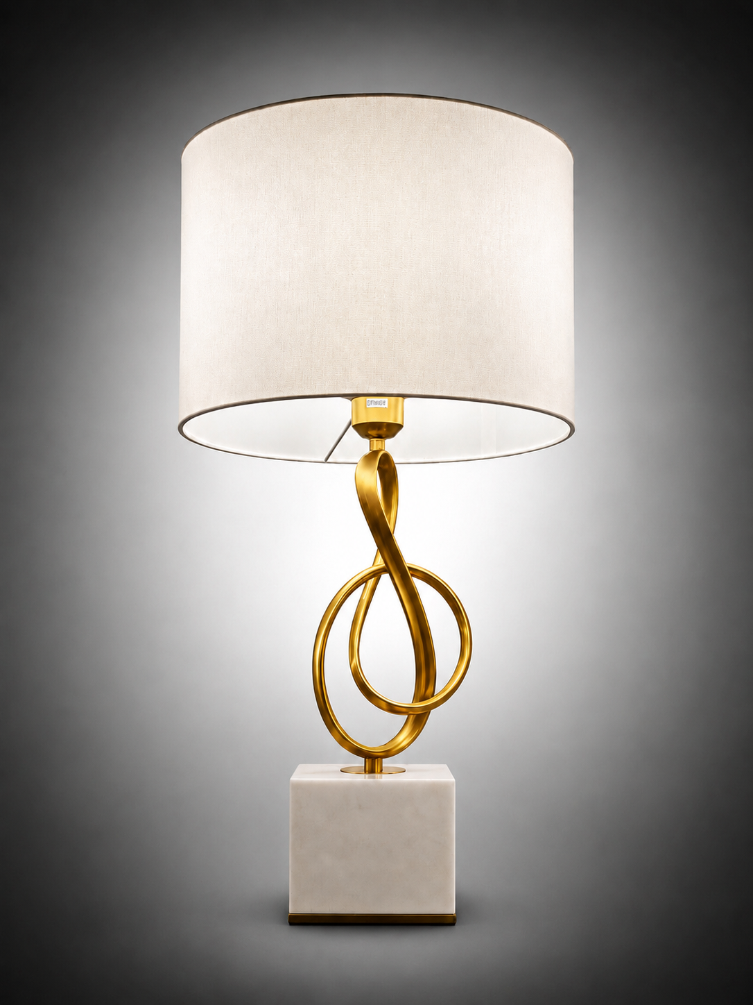 A modern table lamp with a white fabric drum shade, a gold-finished twisted metal base, and a square white marble-like pedestal on a dark gray gradient background.