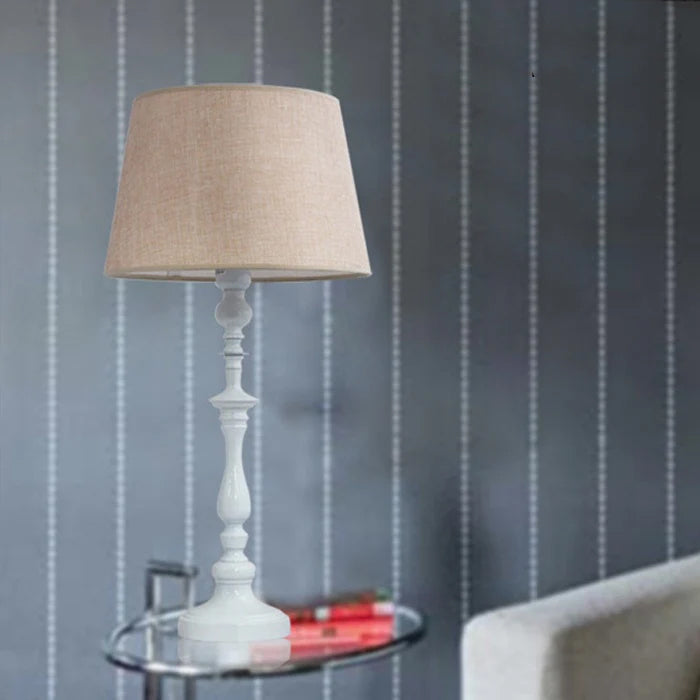 Table lamp with beige shade on a small round table against a striped wall nz