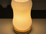 A glowing table lamp with a ribbed, wavy translucent shade and a light wood base, shown lit on a tabletop in a dim interior setting.