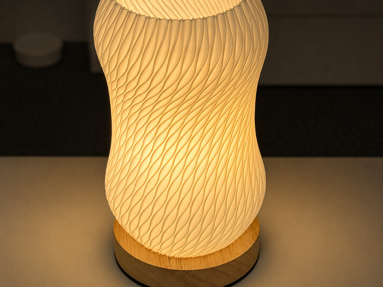 A glowing table lamp with a ribbed, wavy translucent shade and a light wood base, shown lit on a tabletop in a dim interior setting.
