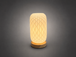 A modern table lamp with a textured, honeycomb-patterned cream-colored shade and a round natural wood base, glowing with a warm light against a dark gray gradient background.