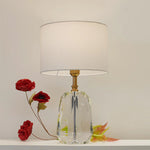 Table lamp with a clear glass base and white shade on the table nz