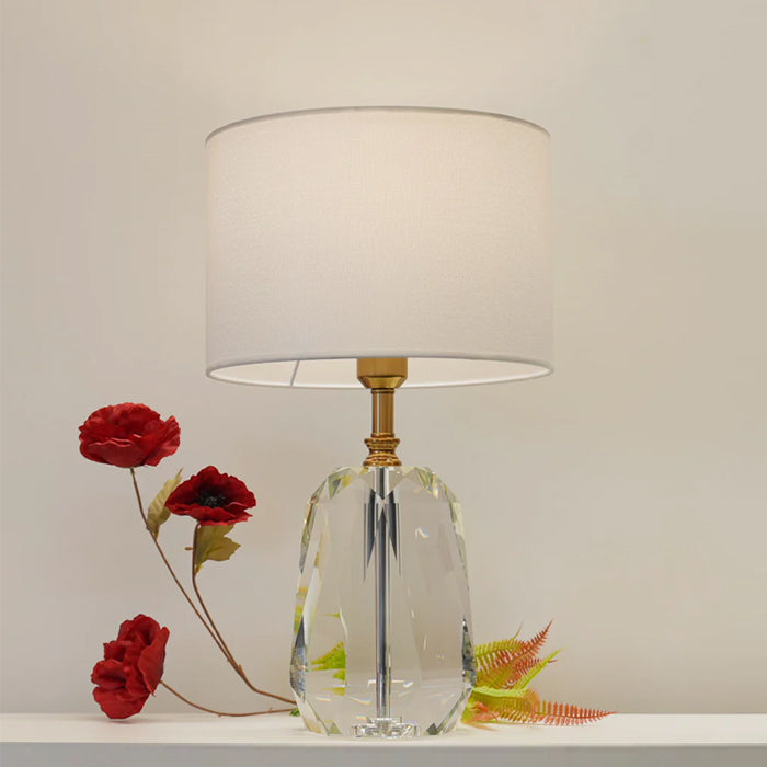 Table lamp with a clear glass base and white shade on the table nz